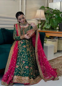 Woman in traditional green and pink embroidered outfit holding a clutch in an indoor setting.Haris Shakeel Formal