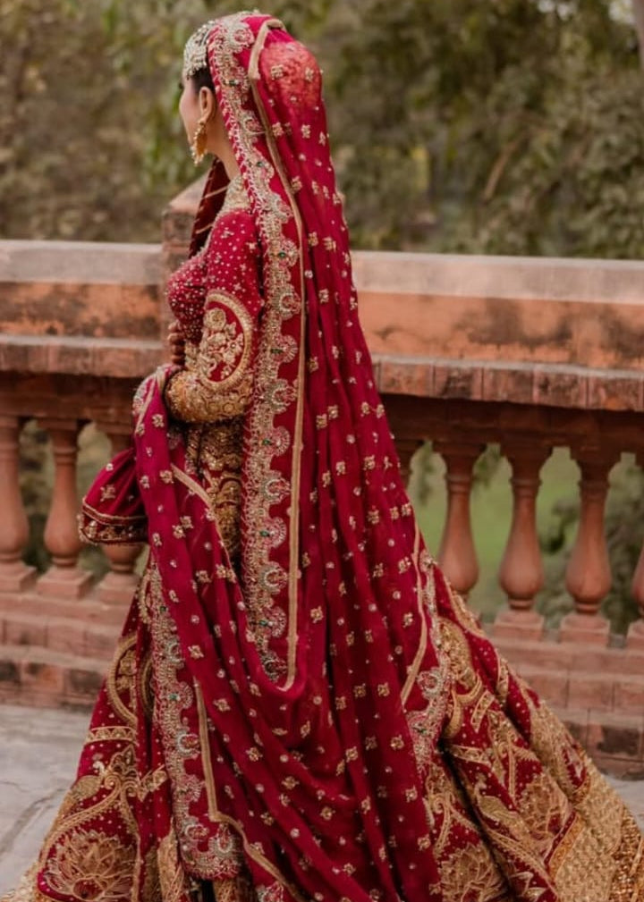 Woman in a red and gold traditional outfit standing on a stone path with greenery in the background